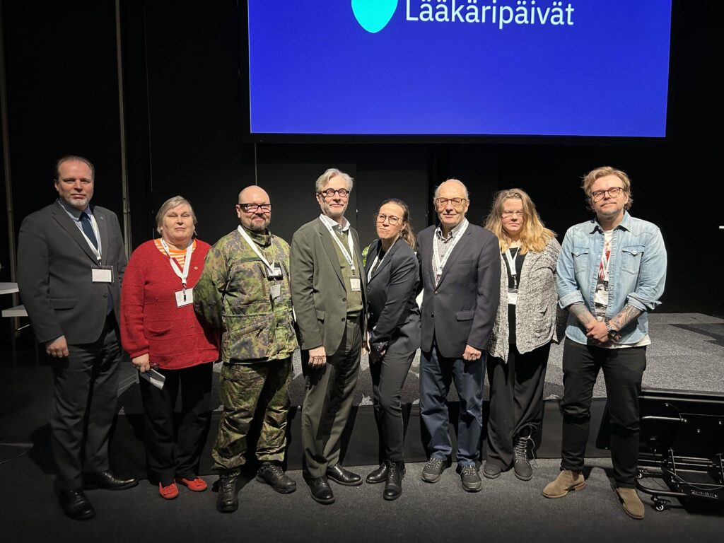 Ryhmä ihmisiä seisoo rivissä luentosalin lavan edessä. Taustalla näkyy Lääkäripäivät-dia.